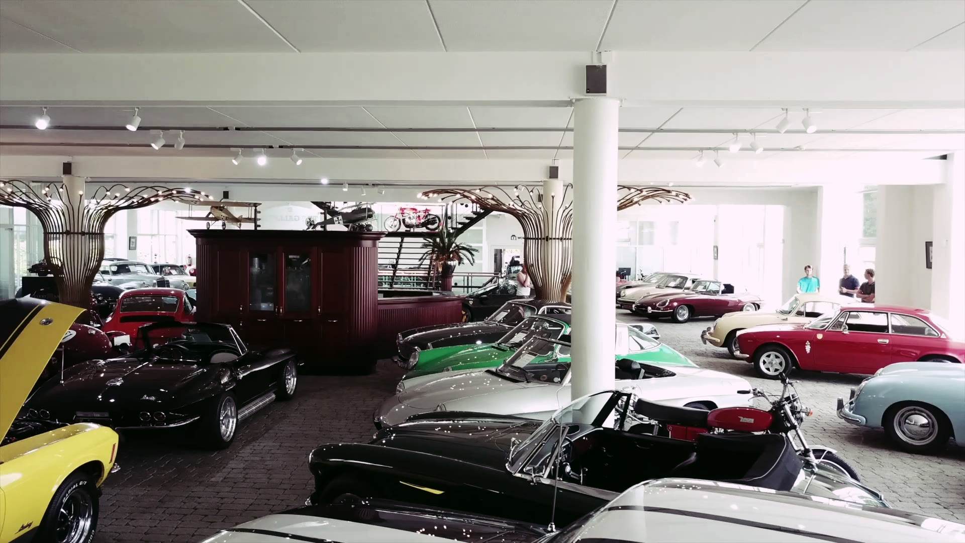 Rows of classic cars on a showroom floor beneath wide circular lights.